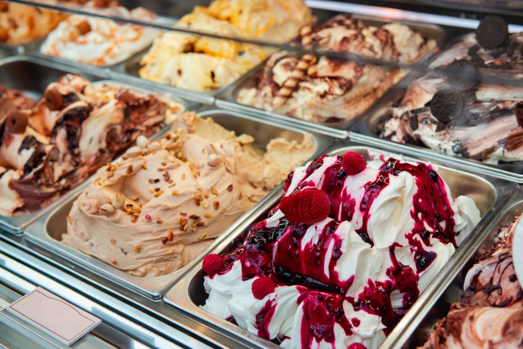 Various flavors of gelato with toppings in a glass display case