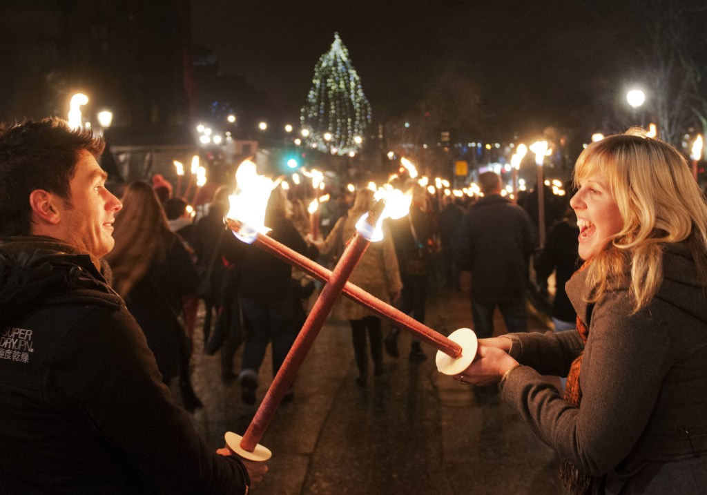 Two people laughing and holding torches as part of a parade procession at night